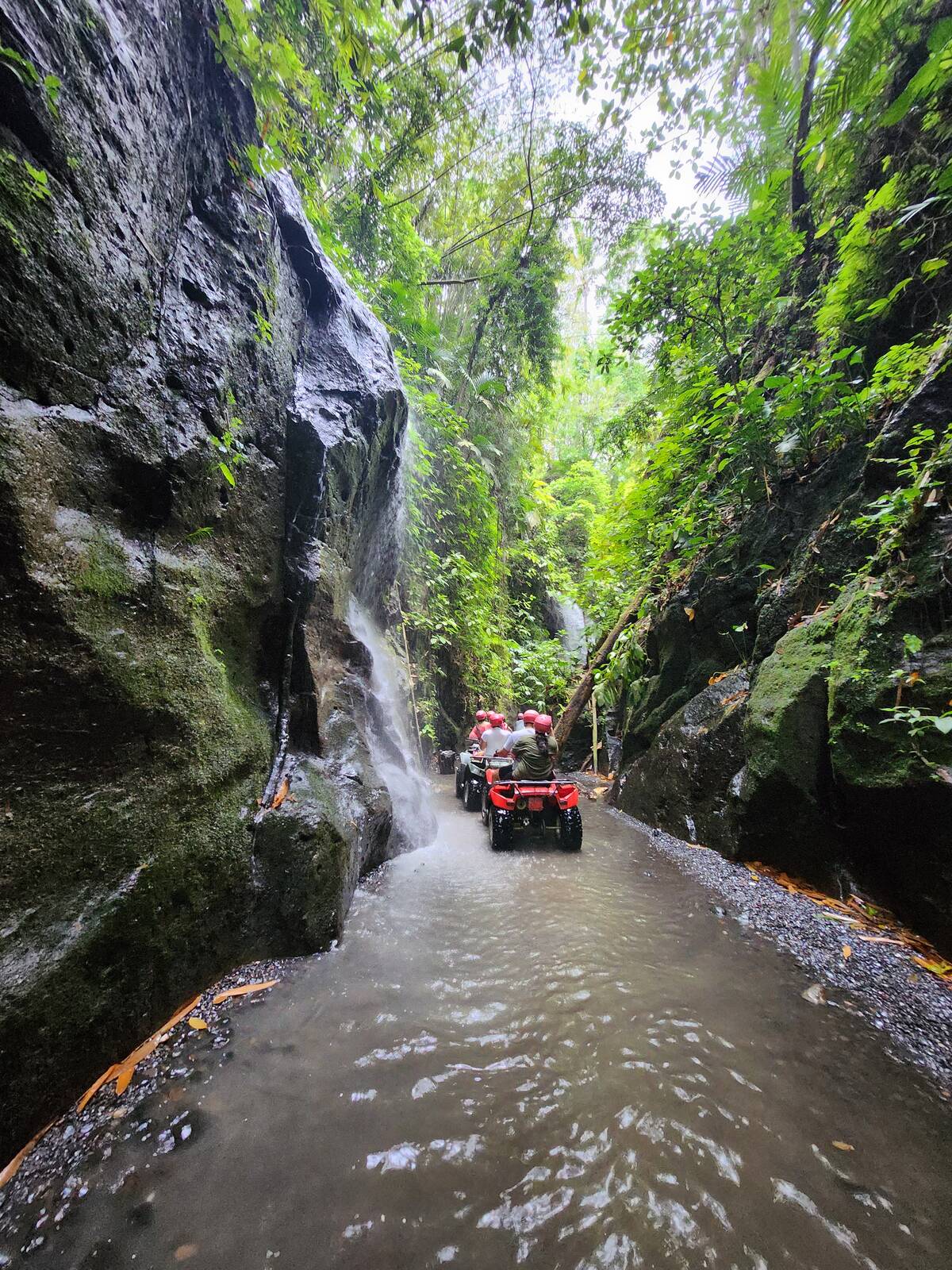 ATV 車隊沿著岩壁瀑布旁的淺水道前進
