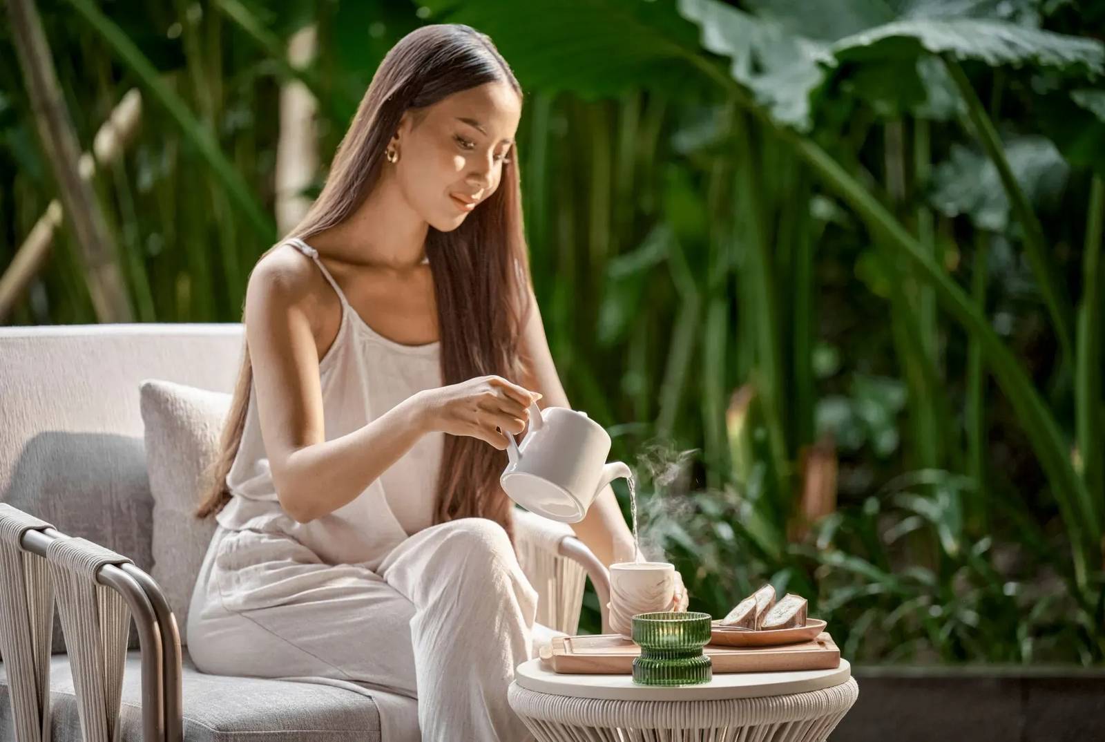 旅客在 Crowne Plaza Labuan Bajo 花園座位倒茶,桌上有茶具與點心