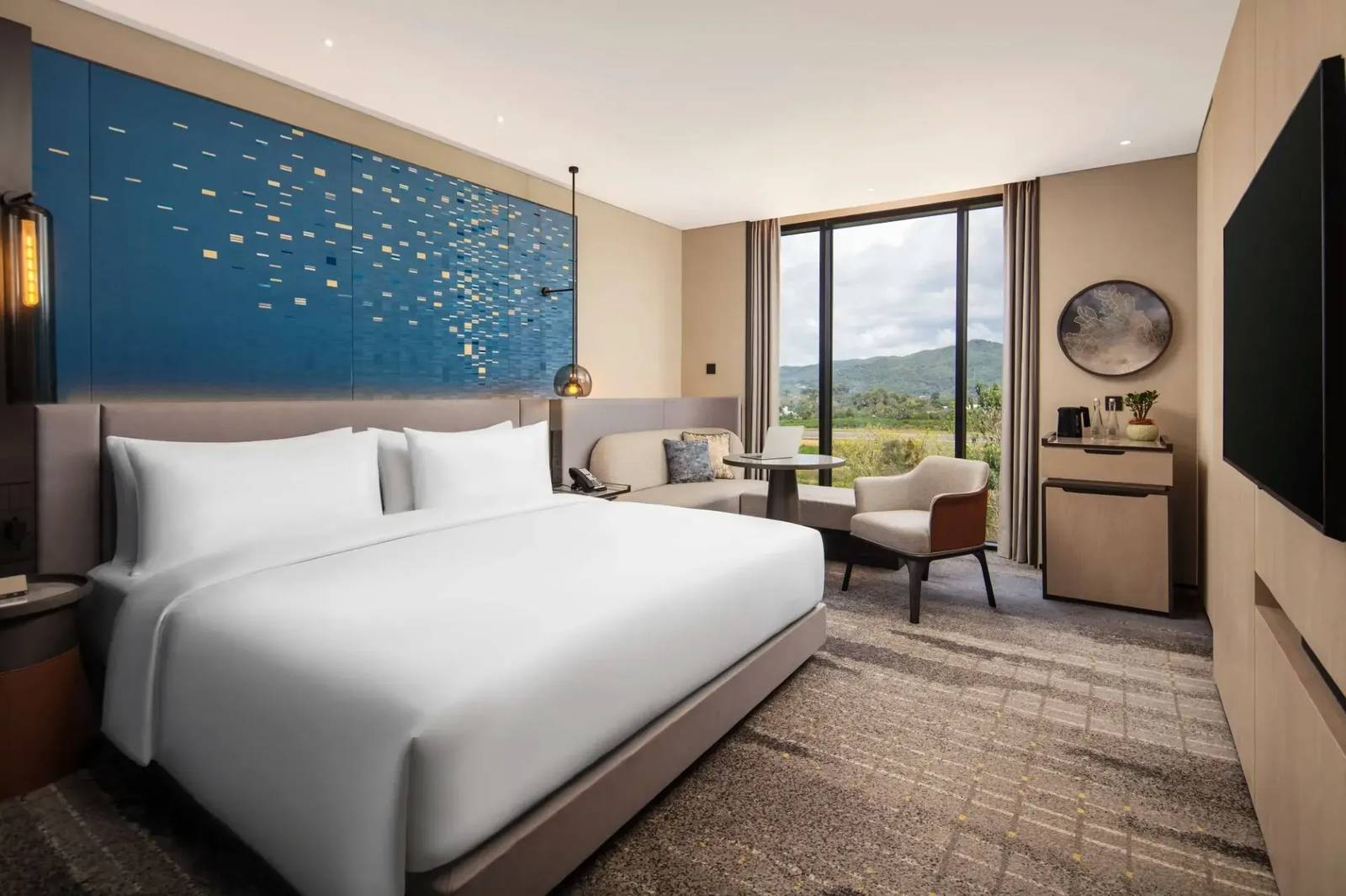 Crowne Plaza Labuan Bajo 客房大床、藍色裝飾牆與窗邊沙發工作區
