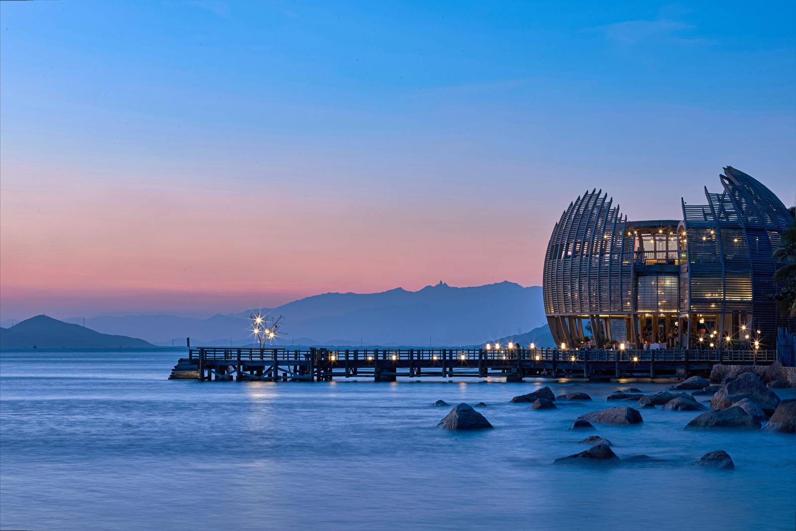 寧凡灣安嵐 Sen 餐廳:黃昏時分立在岩岸的蓮花造型木構建築,棧橋燈火通向海灣