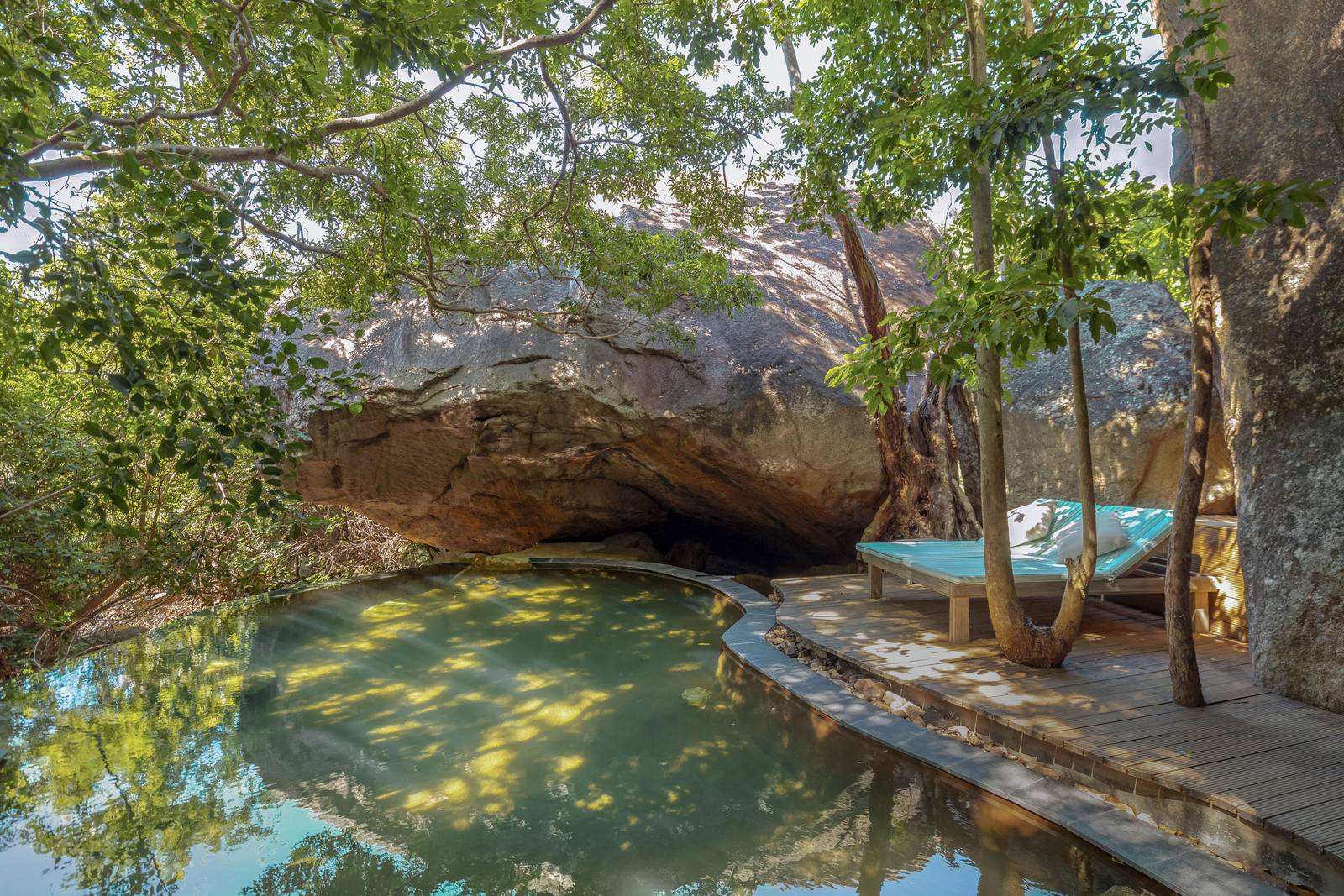 寧凡灣安嵐隱世度假村 Jungle Oasis:巨岩下方的碧綠水池與木甲板躺椅,樹幹穿過甲板