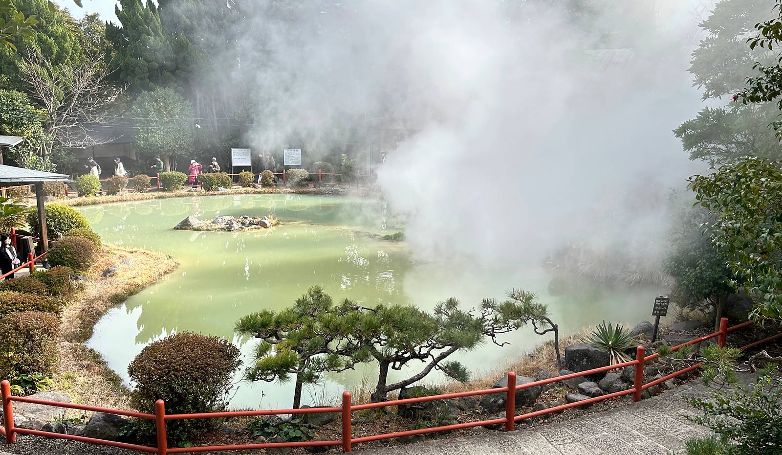 白池地獄淡綠乳白色泉池、湯煙、修剪松樹與紅色欄杆