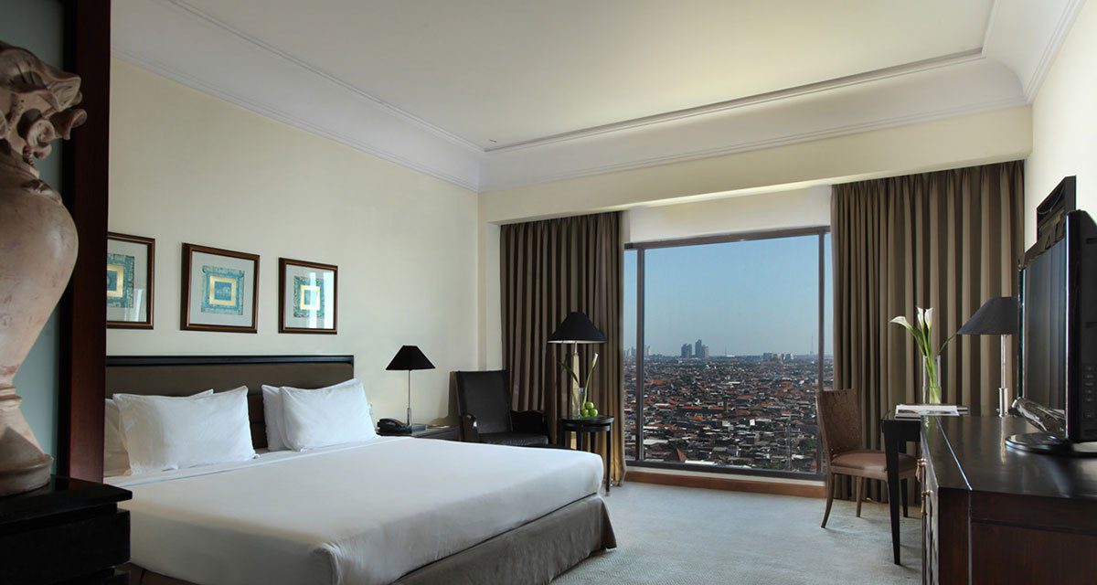 Classic Club Room 的大床與落地窗，窗外可俯瞰泗水市區街景