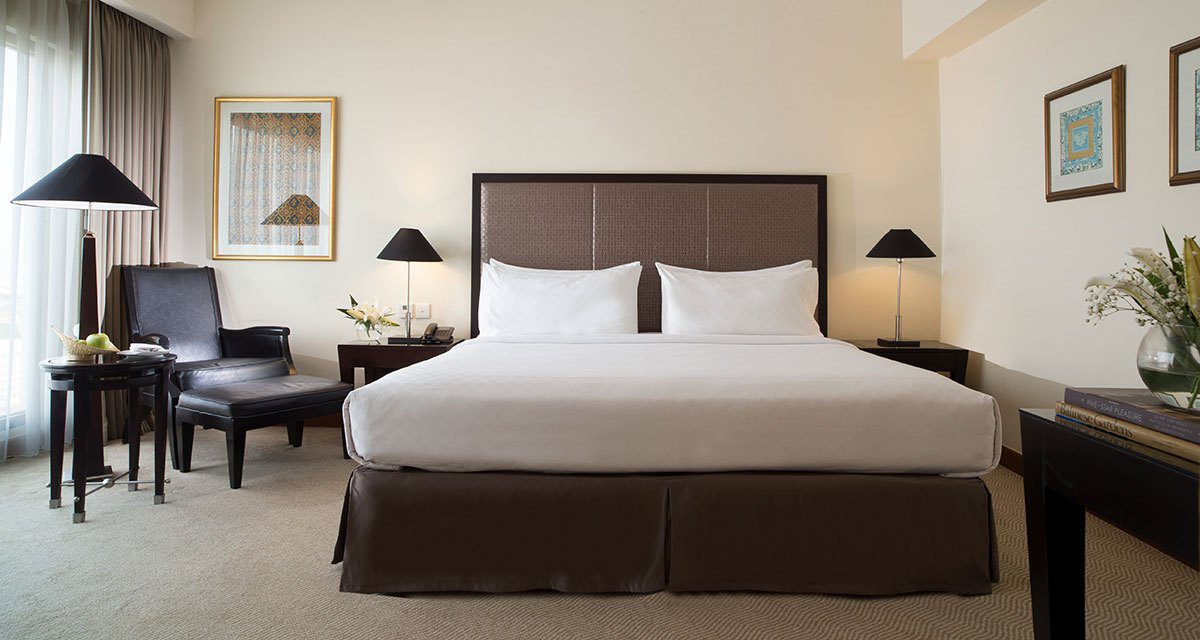 Classic Room 的大床、床邊閱讀椅與工作桌，房內以中性色調布置