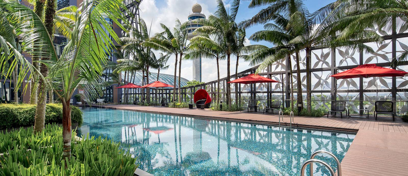 Crowne Plaza Changi Airport 戶外泳池、紅色陽傘、棕櫚與後方塔台