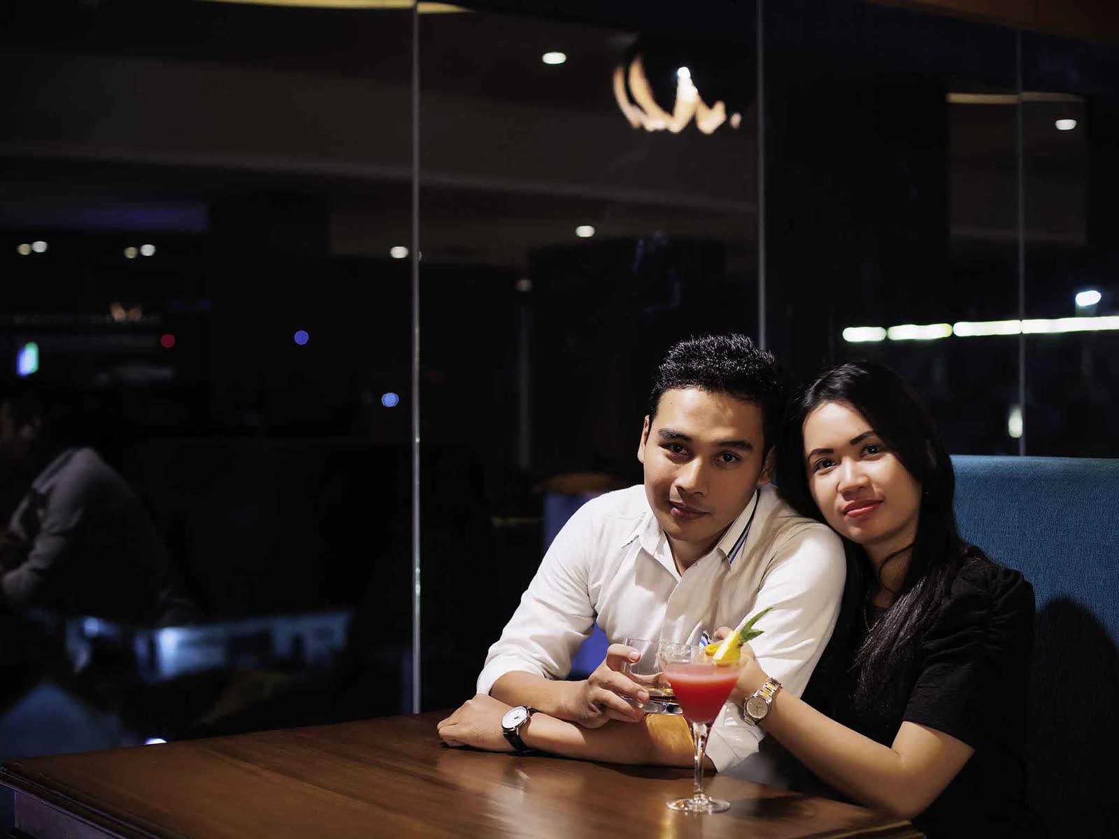 日惹 Adi Sucipto 美爵酒店昏暗酒吧桌前一對客人,桌上有馬丁尼杯與冰塊杯