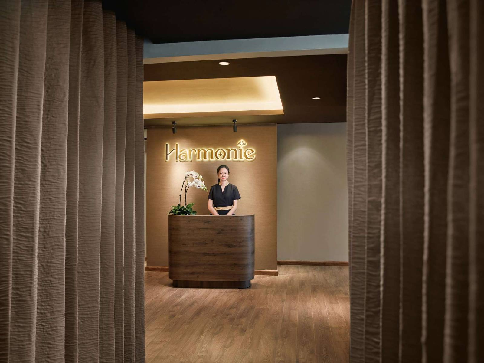 河內歌劇院酒店 Harmonie 水療接待櫃台，深色弧形桌、白色蘭花與牆上招牌
