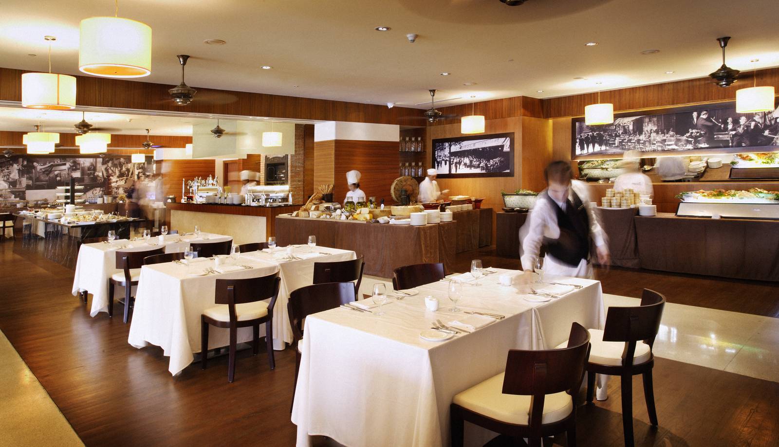 河內西湖洲際酒店 Café du Lac，白桌布方桌、木護牆與後方自助檯，工作人員穿白襯衫深色背心走過