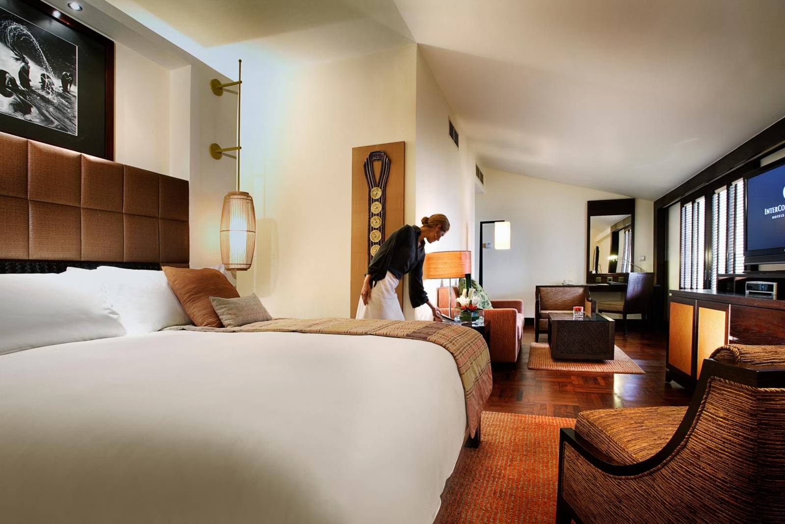 河內西湖洲際酒店 Junior Suite，前方大床與皮革床頭，後方橙椅、咖啡桌與深色木百葉窗