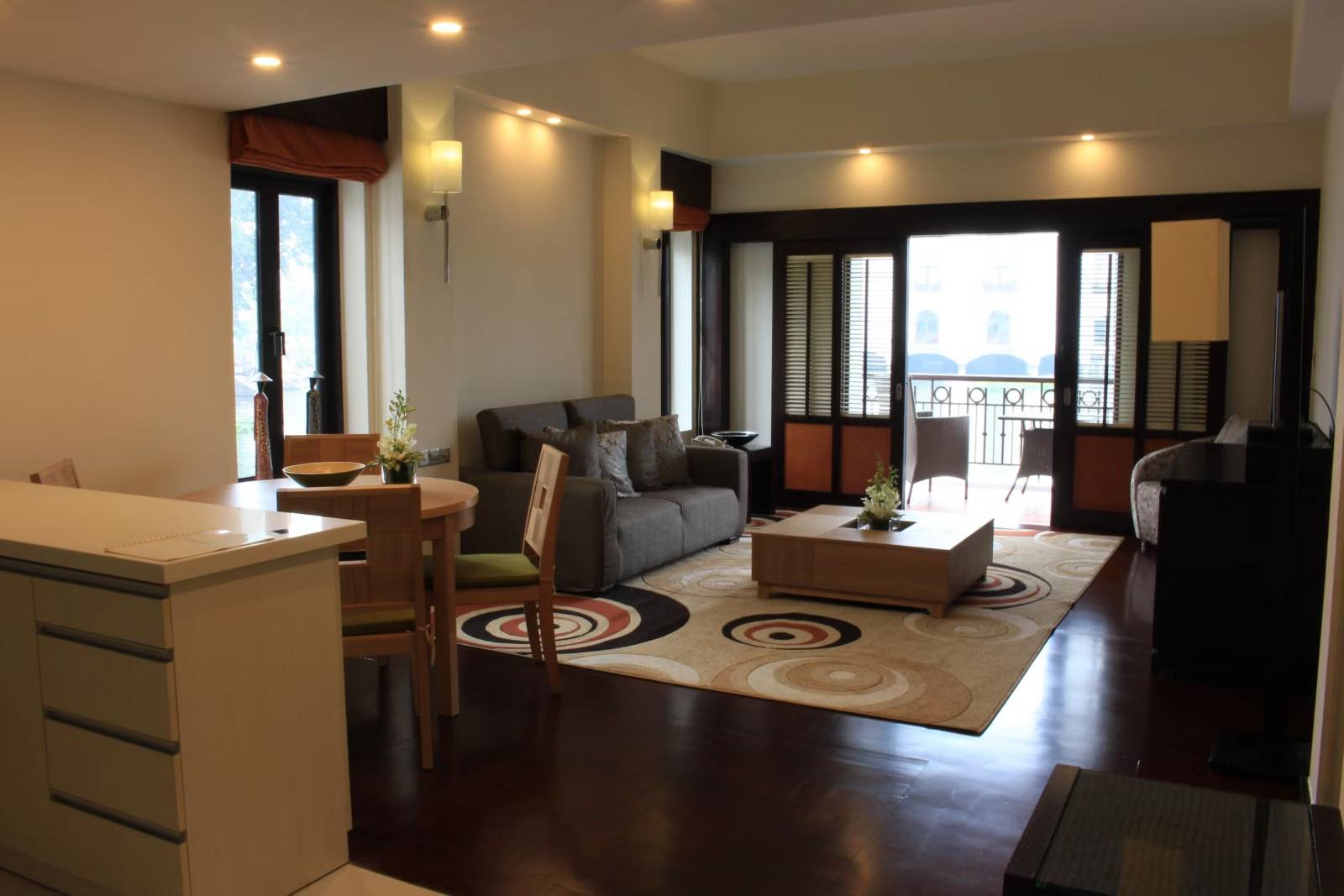 河內西湖洲際酒店水上 Residence 起居，灰色沙發、圓桌兩椅與淺木茶几，落地窗通向有藤椅的陽台