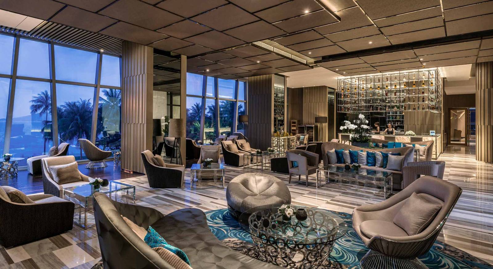 芽莊洲際酒店 Lobby Lounge 黃昏時分，落地窗望向棕櫚與海灣，後方可見吧檯酒架