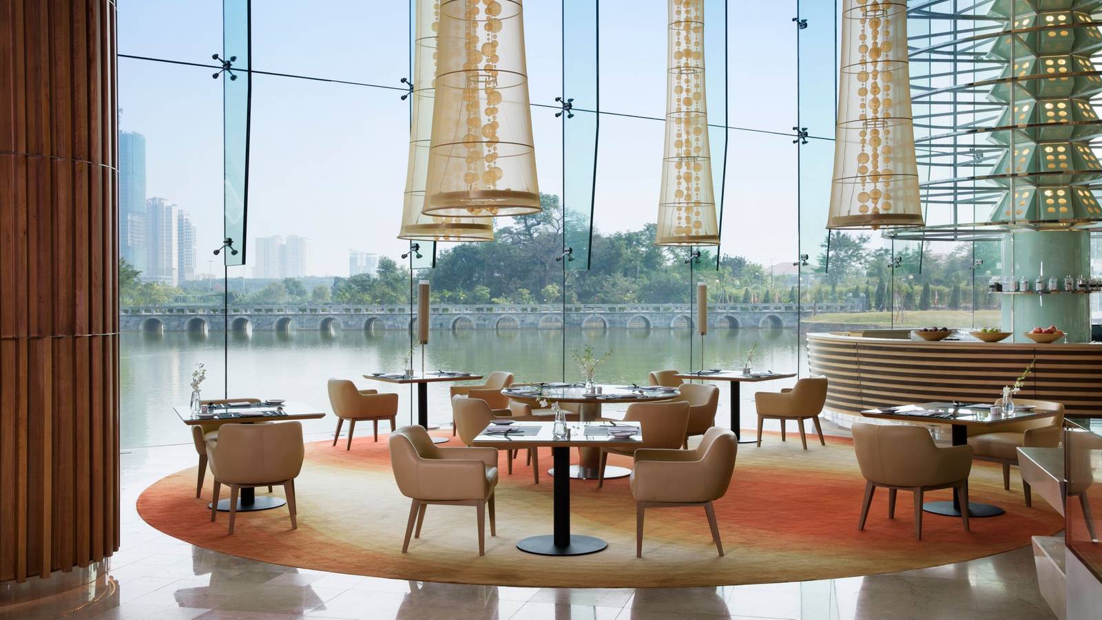 河內 JW 萬豪酒店 JW Café,金色圓柱吊燈、餐桌椅與落地窗外的石拱橋與湖面
