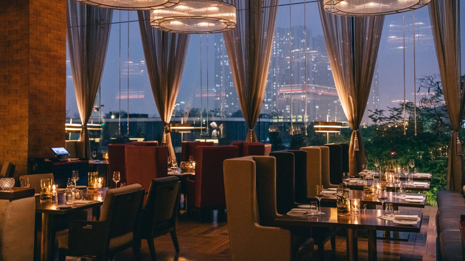 河內 JW 萬豪酒店 French Grill 夜間餐廳,燭光餐桌、高背椅與落地窗外的城市暮色