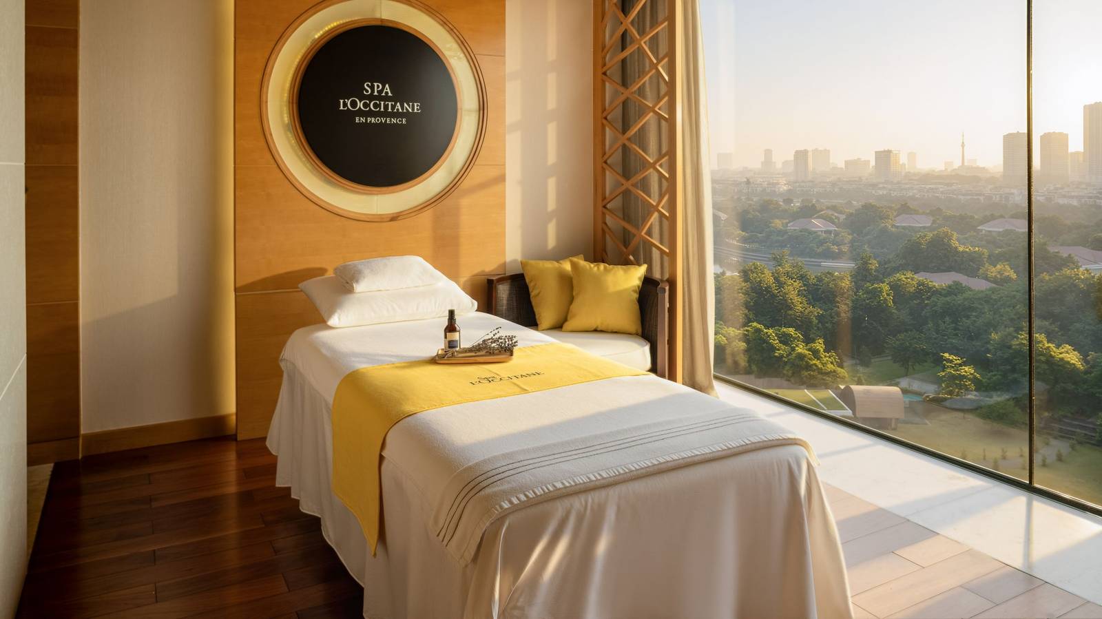 河內 JW 萬豪酒店 Spa L'Occitane 護理室,按摩床、圓形品牌燈箱與落地窗暮色城景