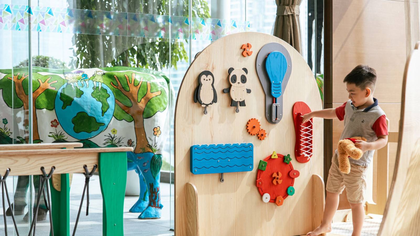 河內 JW 萬豪酒店 Kids Café 遊戲區,兒童在拱形木製感官牆前玩耍,旁有彩繪牛雕像
