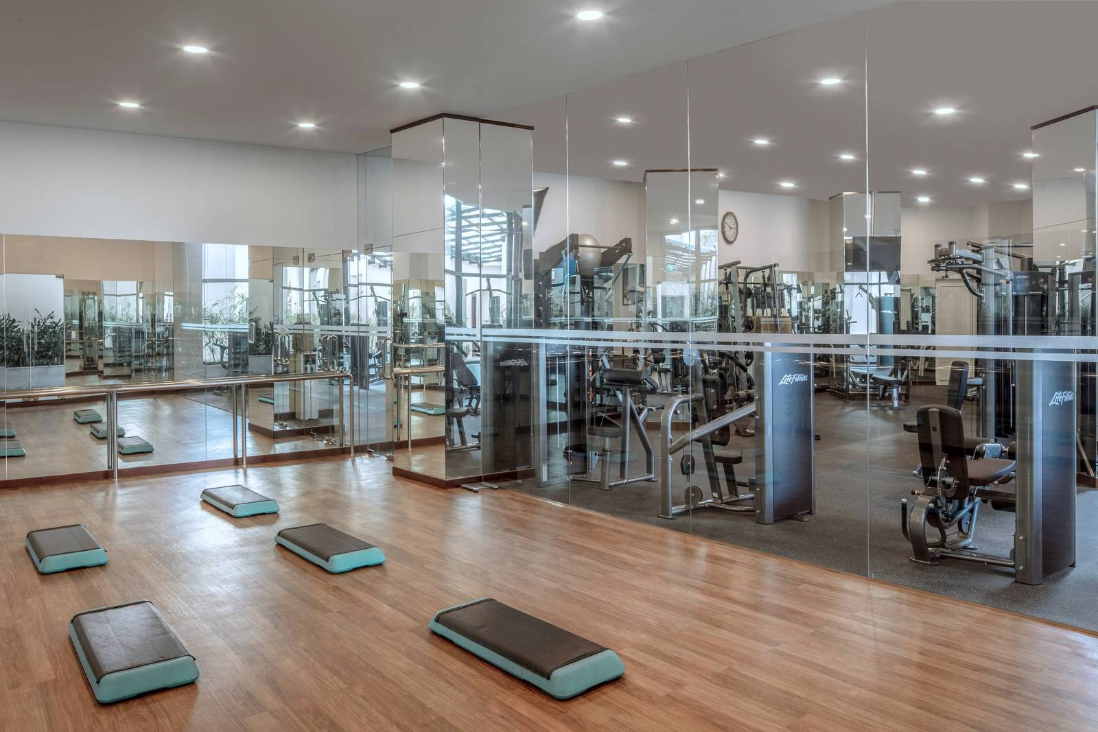 河內美利亞酒店健身房:前方木地板與踏階,玻璃隔間後是 Life Fitness 重訓器材與鏡面柱