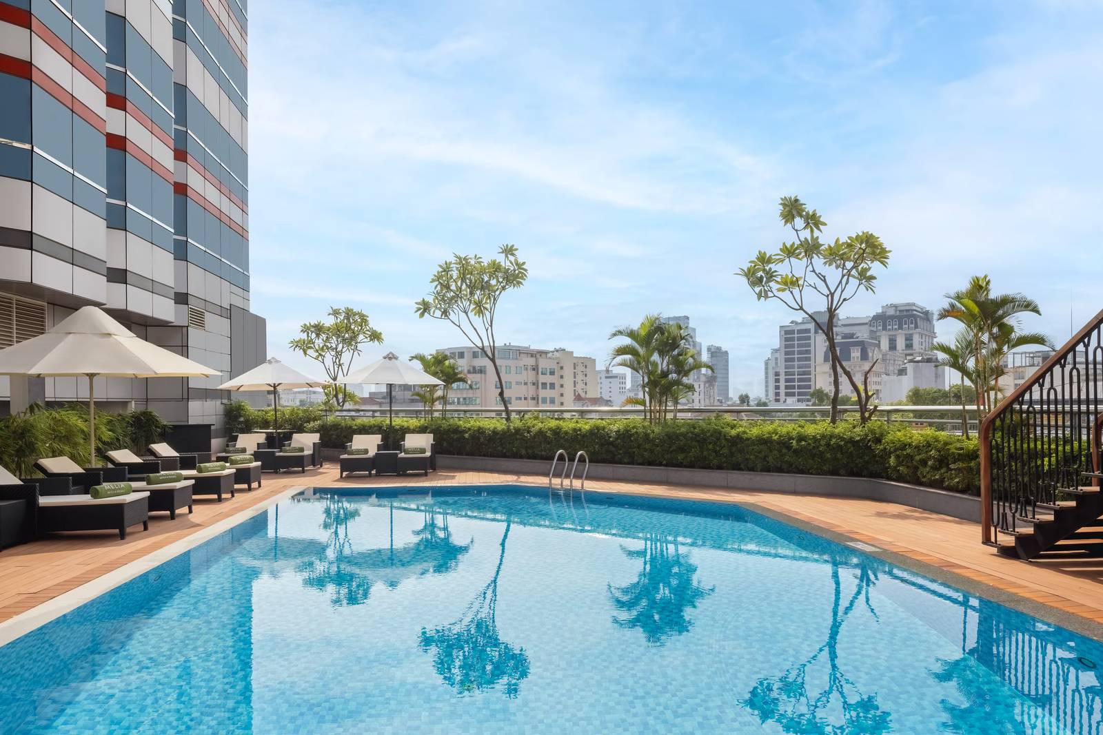 河內美利亞酒店屋頂泳池:藍色長池、白傘、躺椅上的 MELIÁ 綠巾,後方是河內樓群