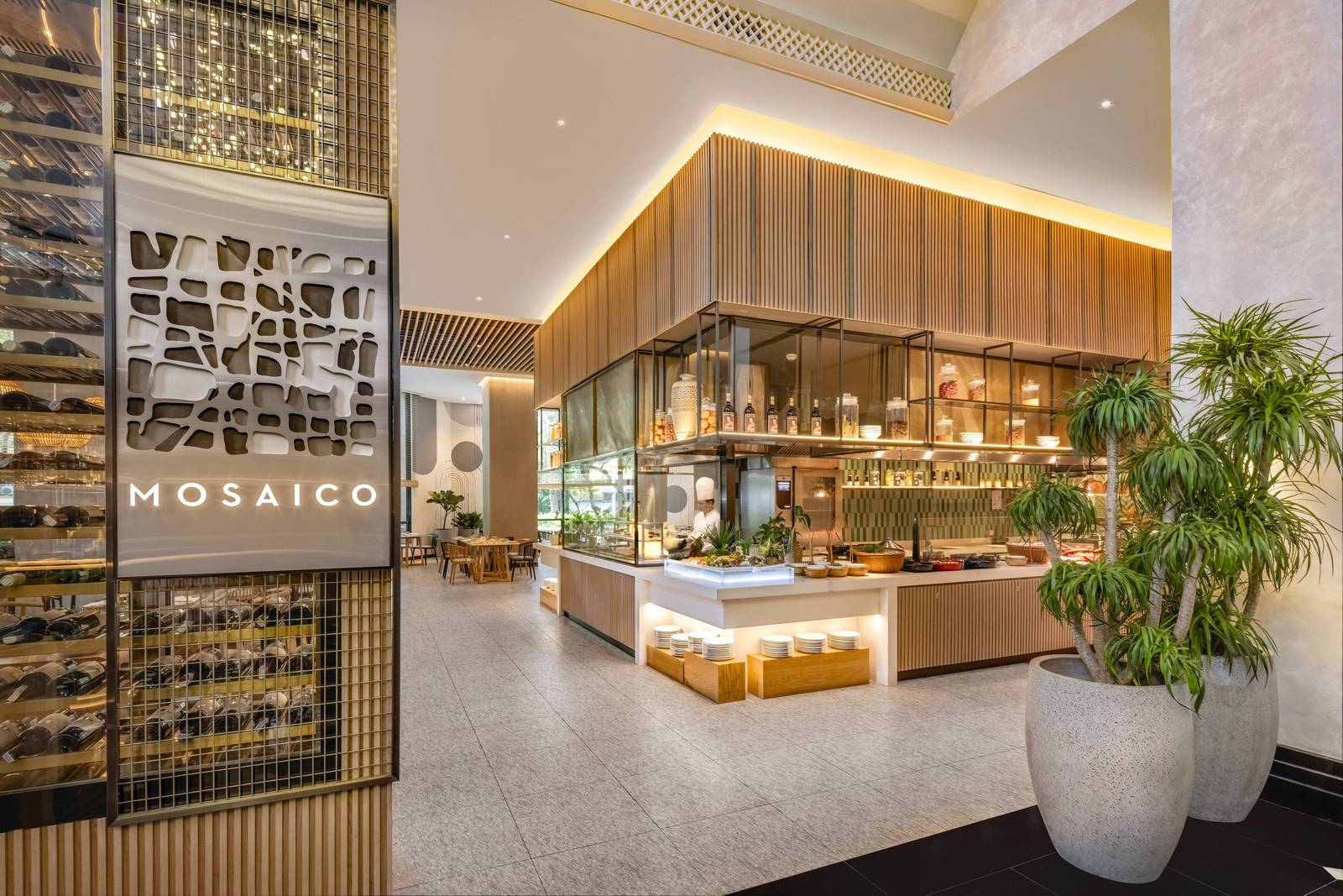 河內美利亞酒店 Mosaico:左側金屬 MOSAICO 立牌與酒瓶架,中央為木格柵吊頂的開放廚房與自助檯