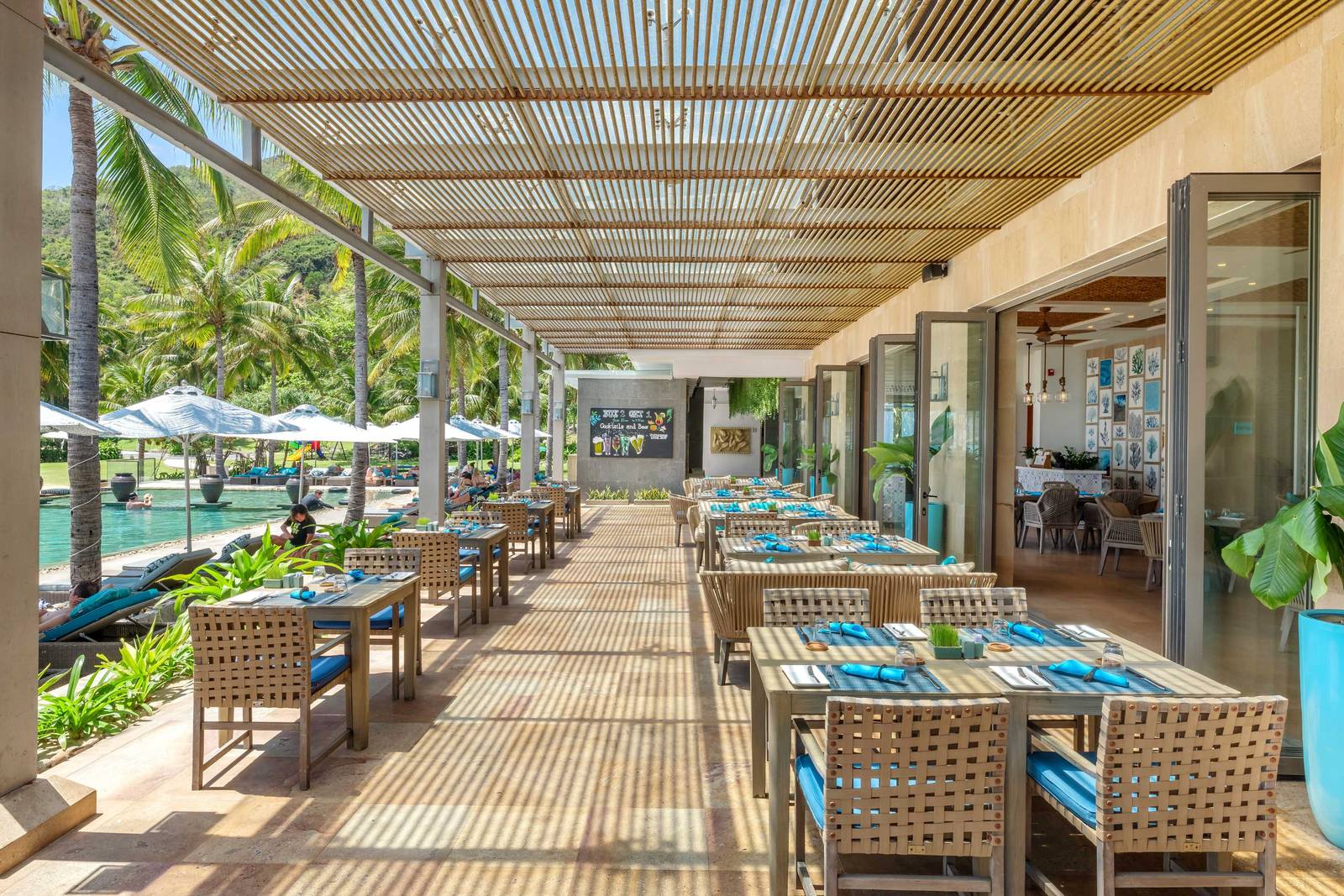 芽莊 Mia 度假村 Kitchen By The Sea 戶外木構餐廳,藍白色餐桌面向海面與綠坡
