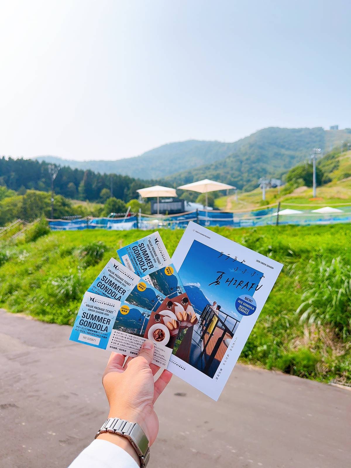 手持比羅夫夏季纜車套票與活動摺頁，背景為綠色山坡