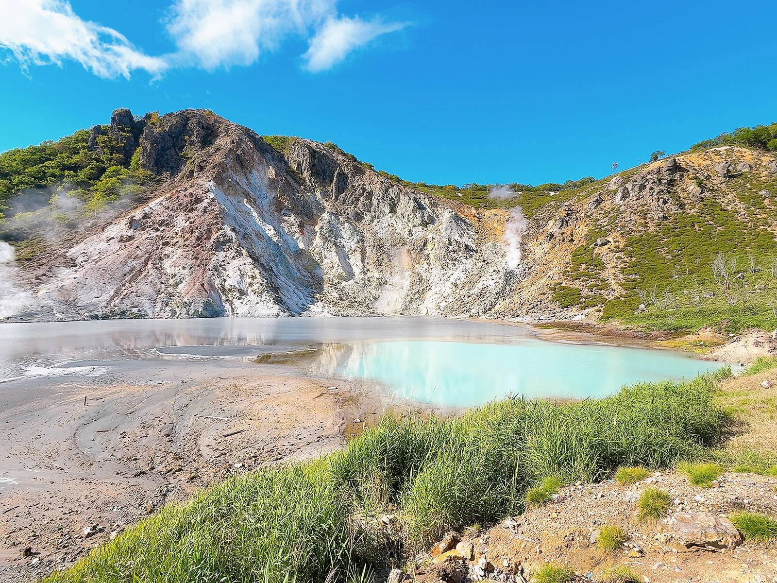 大湯沼的淡青色與灰色水面，後方日和山岩坡升起白色噴氣