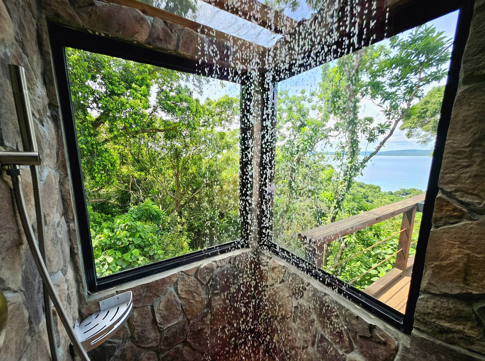 帛琉卡羅琳度假村帆布帳石砌雨淋，落地窗外是熱帶林木、木欄杆與遠方海灣島影