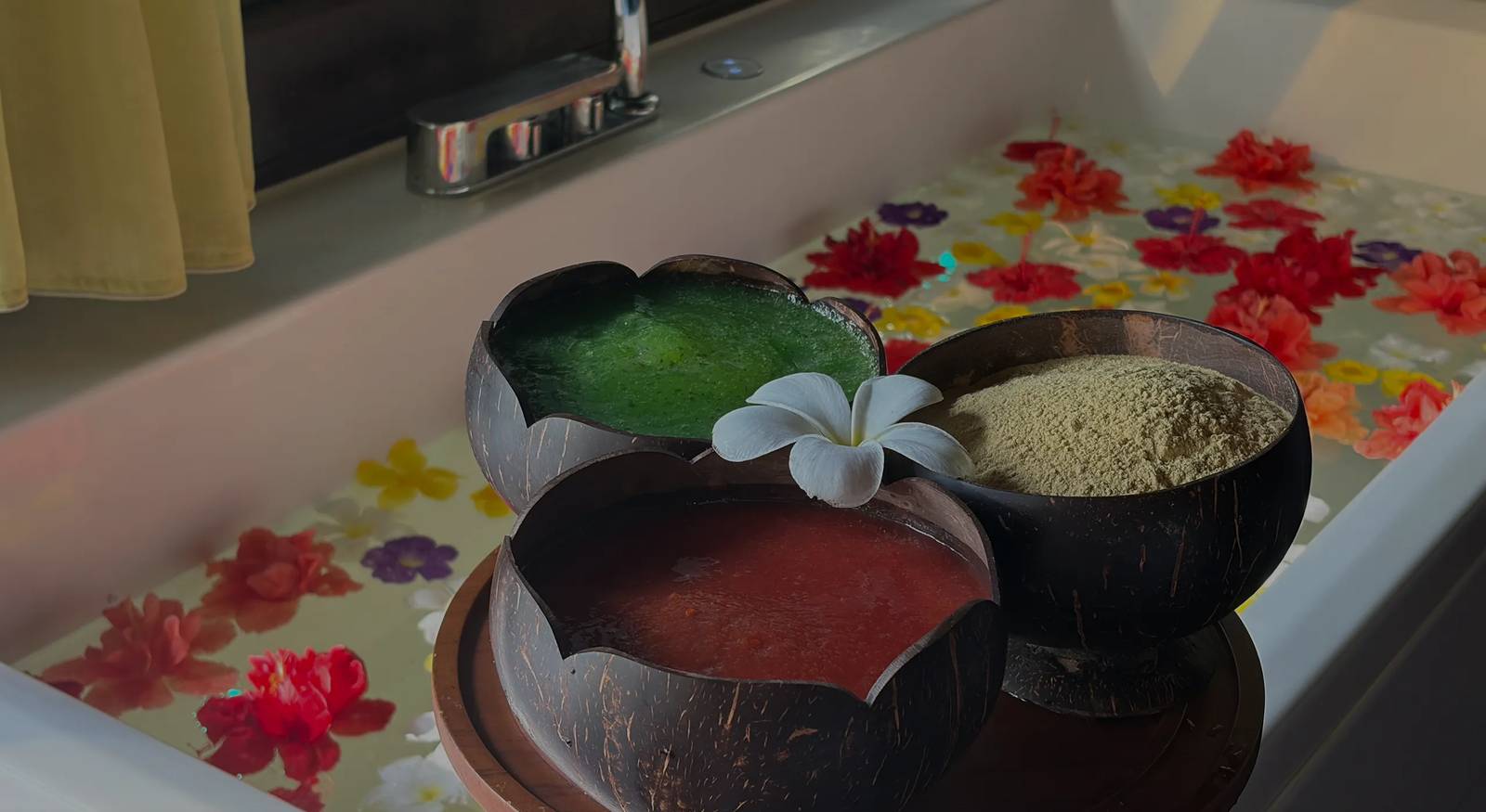 Elilai Spa 浴池邊三只椰殼碗盛著綠、橙、米色護理膏,白雞蛋花與花瓣浮在水面