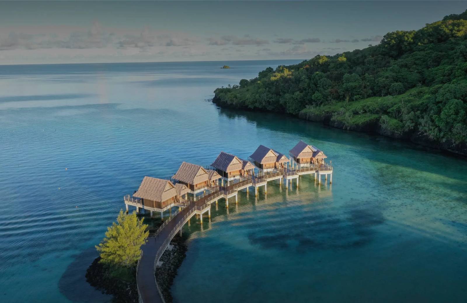 The Pristine 水上平房空拍:五棟尖頂 bungalow 沿木棧道排入清澈潟湖