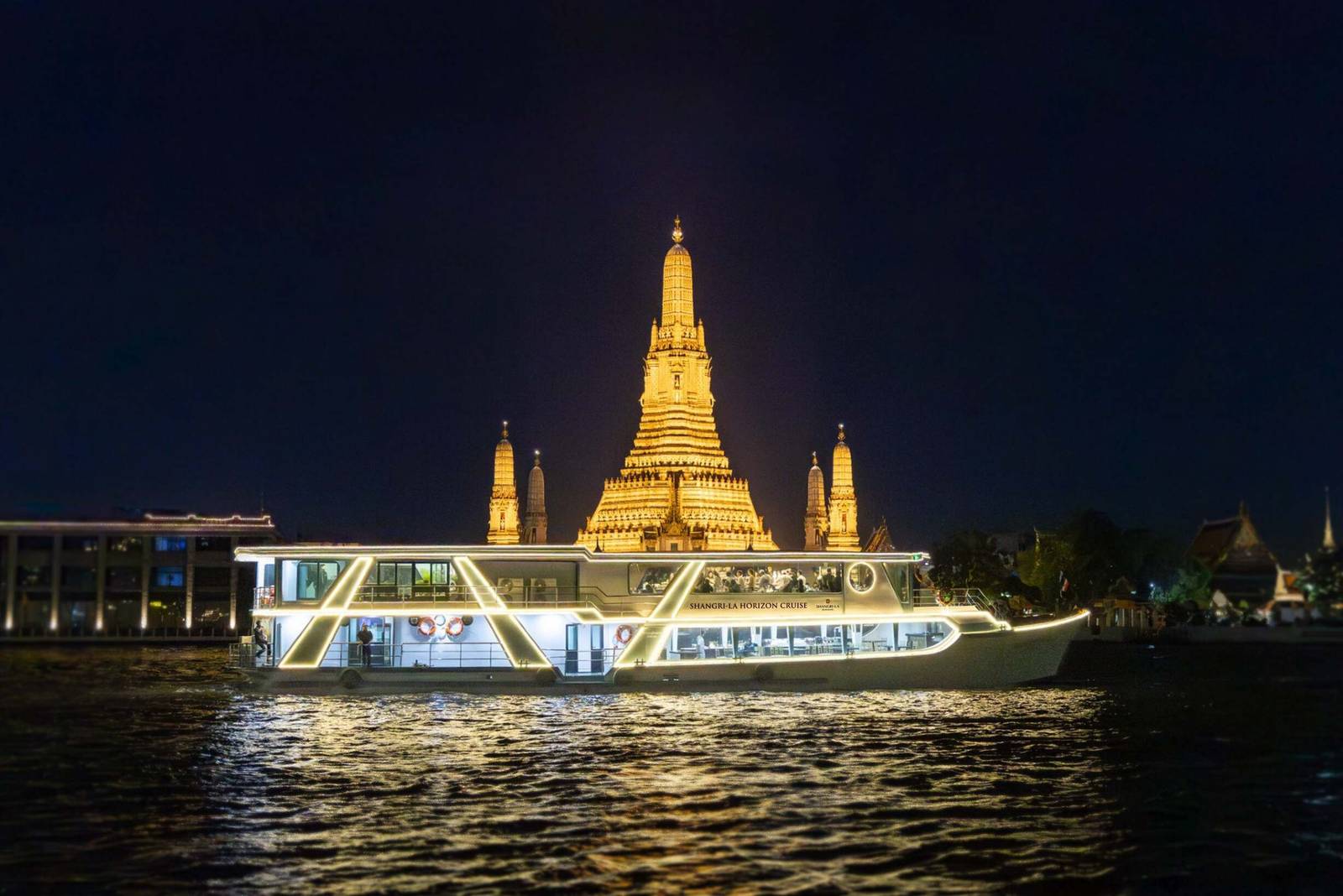 夜色中白色雙層「SHANGRI-LA HORIZON CRUISE」遊船亮燈駛過昭披耶河，後方是金黃色燈光的鄭王廟主塔與副塔