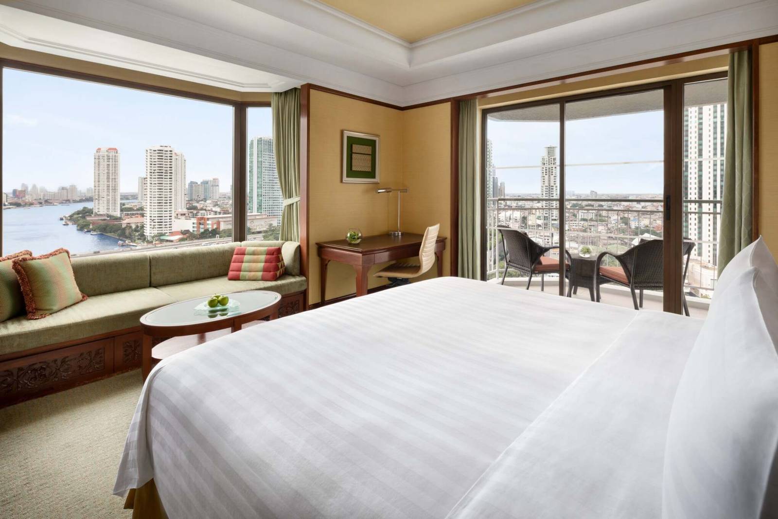 曼谷香格里拉酒店 Premier Balcony 客房：窗邊sage綠長沙發與玻璃茶几，書桌與河景陽台藤椅，窗外是昭披耶河與對岸高樓