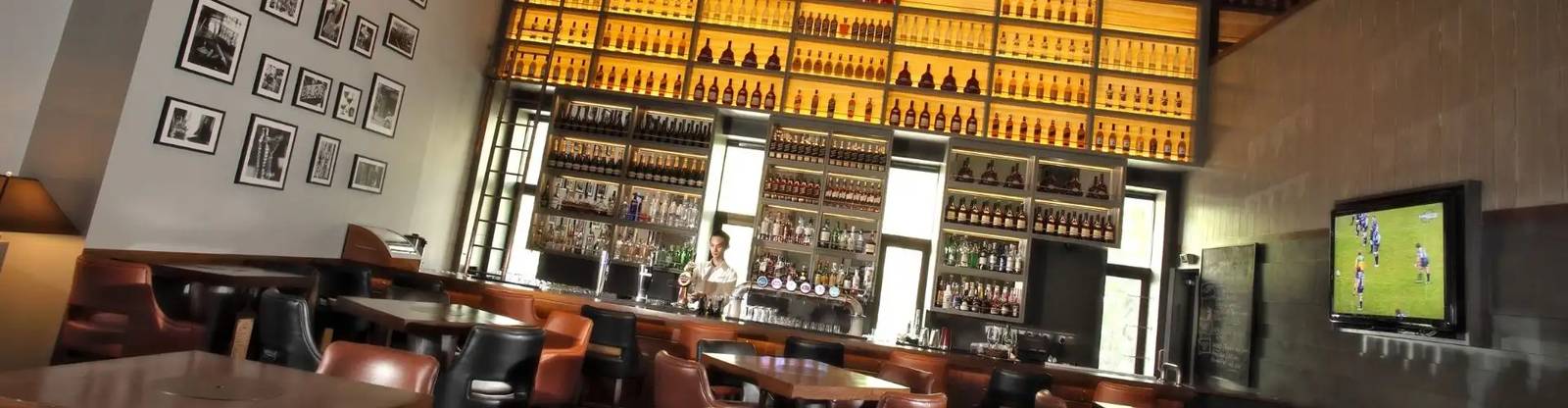 吉隆坡香格里拉 Arthur's Bar & Grill，深色吧台後方整面背光酒瓶架，皮革座椅面向吧台