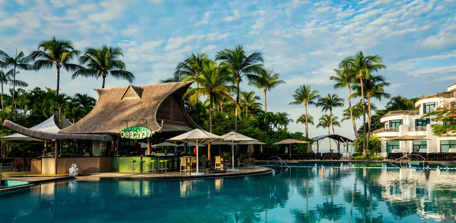 新加坡聖淘沙香格里拉度假村 Siloso Beach Bar：茅草頂酒吧立於主泳池邊，綠色吧檯與高腳椅，後方是陽台客房樓