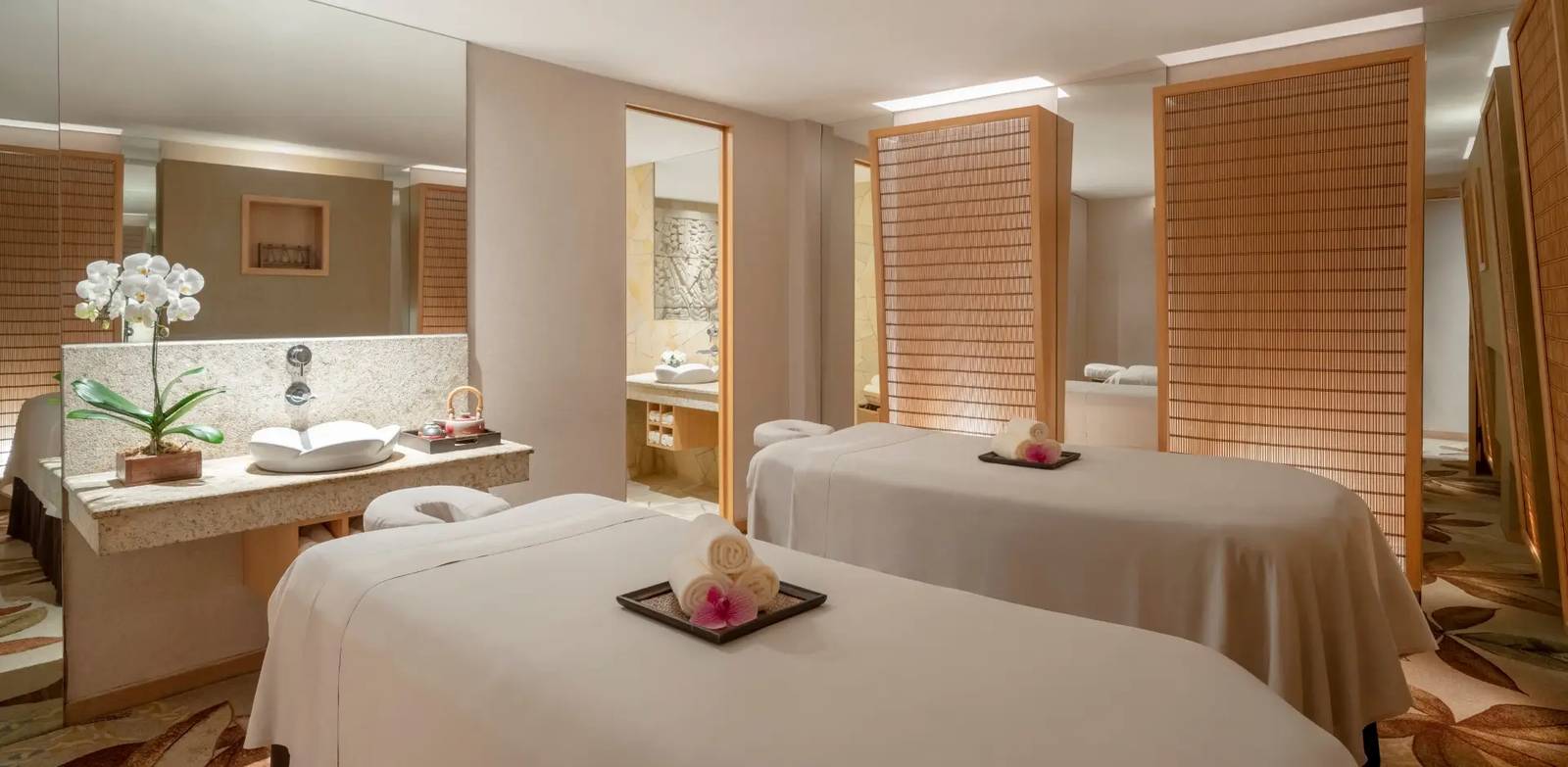 新加坡聖淘沙香格里拉度假村 Chi, The Spa 雙人療程室：兩張鋪白巾的按摩床、花形洗手台與木質摺屏