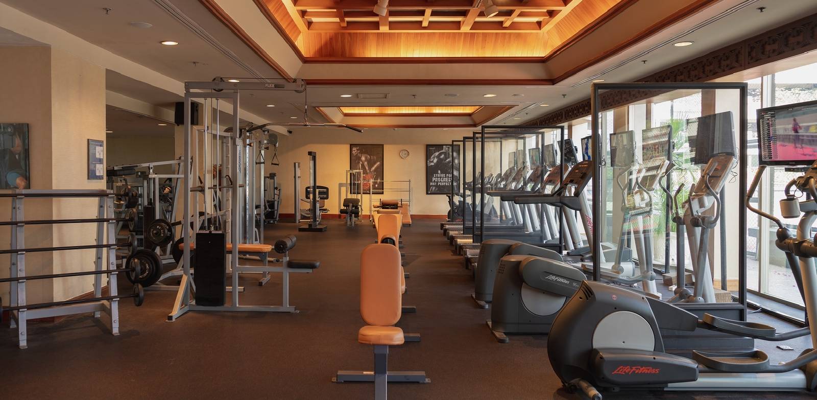 泗水香格里拉酒店健身中心有 Life Fitness 橢圓機與跑步機、重量器材，木格天花板與落地窗外的綠意