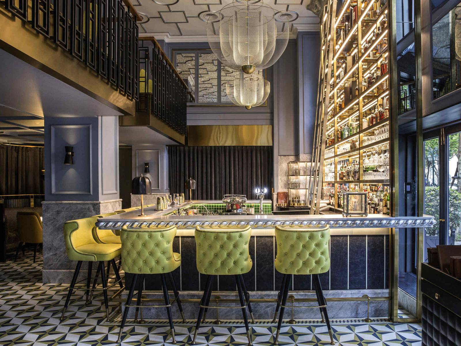 河內索菲特傳奇大都會酒店 angelina 酒吧,大理石吧台、草綠色高腳椅與通頂金色酒架
