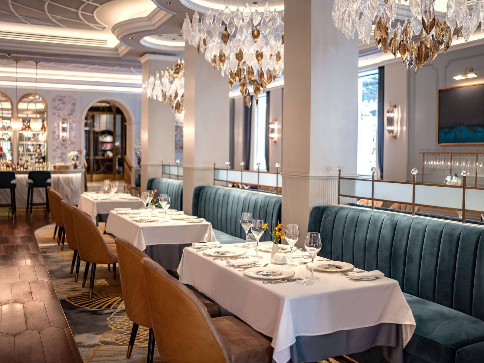 河內索菲特傳奇大都會酒店 Le Beaulieu 餐廳,白桌布、藍綠絨沙發、葉片造型吊燈與淺色圓柱