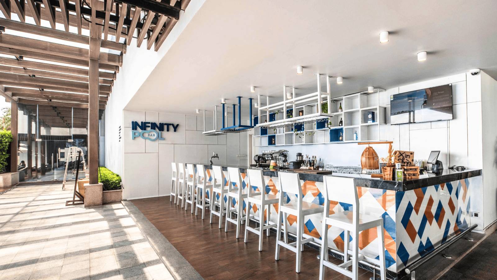 芽莊珍珠海濱酒店 Infinity Pool Bar 白藍橘幾何吧台、白色高腳椅與牆上英文店名