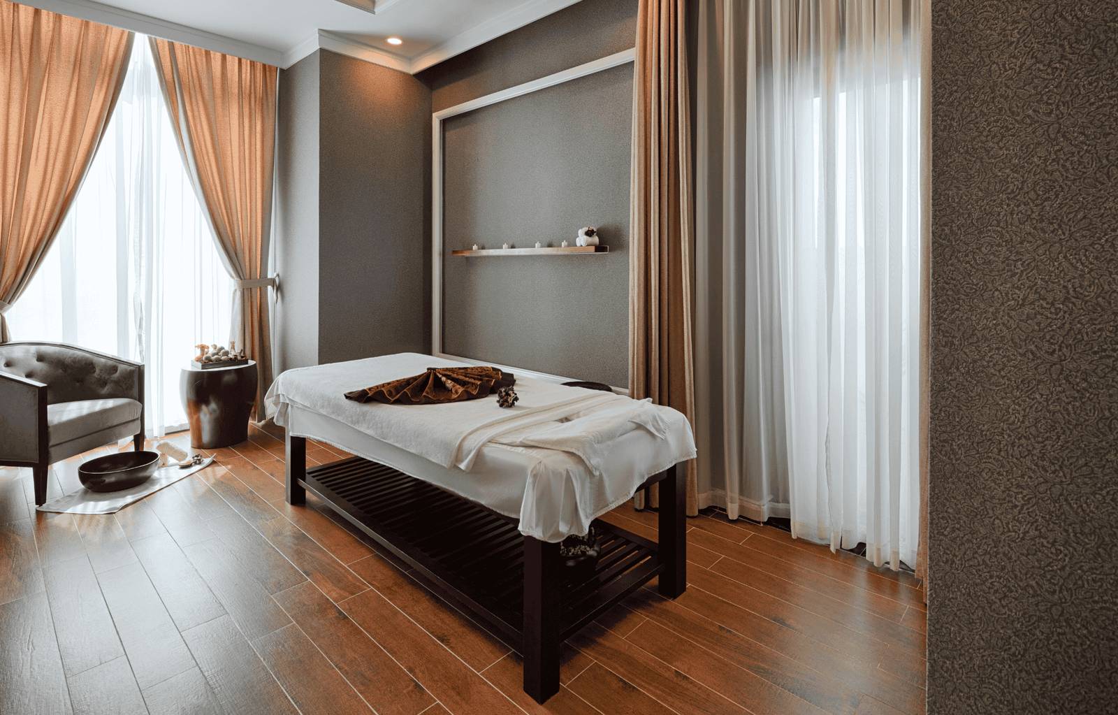 芽莊珍珠海濱酒店 Vincharm Spa 單人護理室,白色床單按摩床、木地板與落地窗紗簾