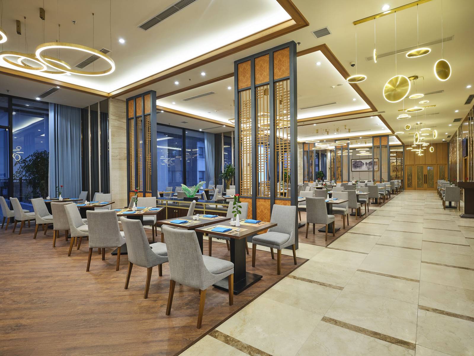 下龍灣溫德姆傳奇酒店餐廳方桌灰椅、木格柵隔間與環形吊燈,桌上藍餐巾