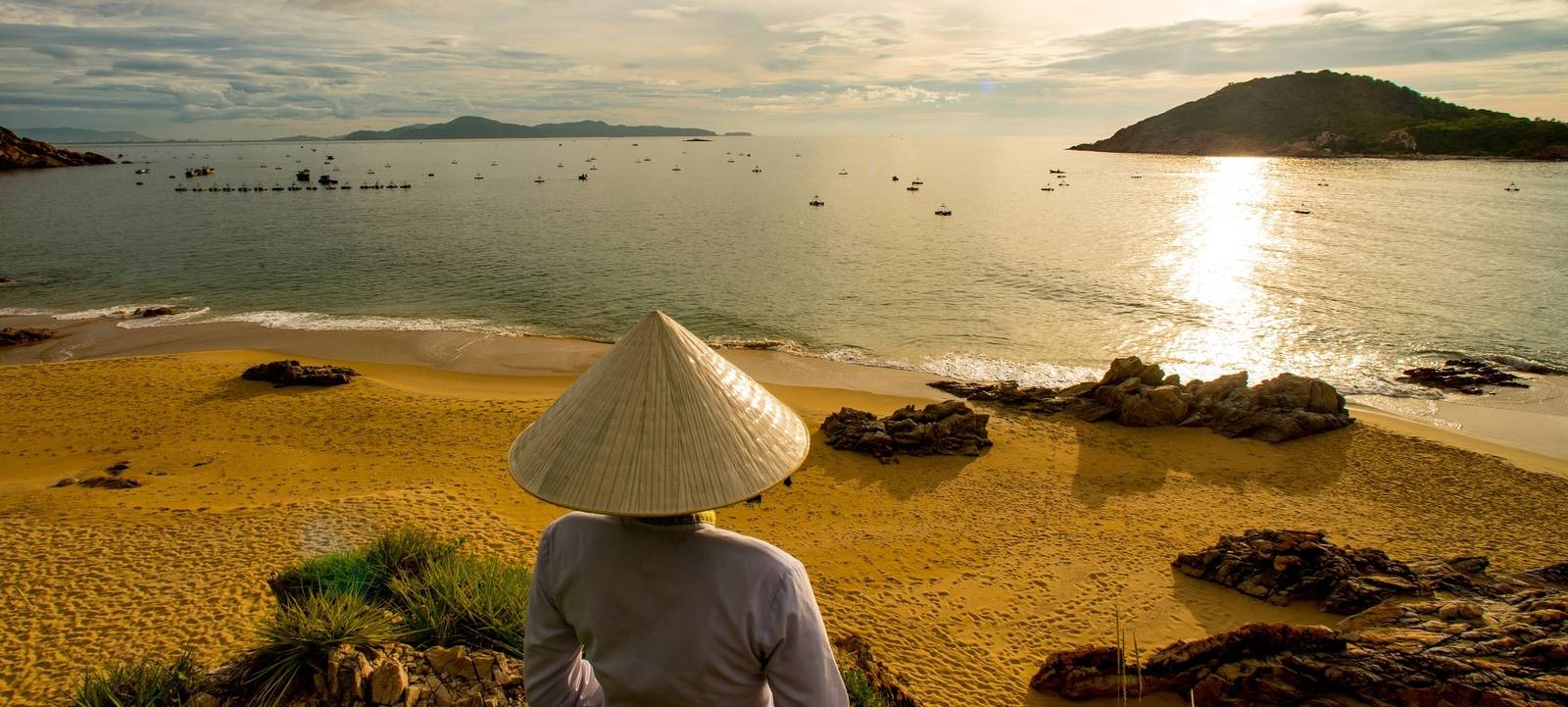 戴斗笠的人坐在岩石上看海灣日出