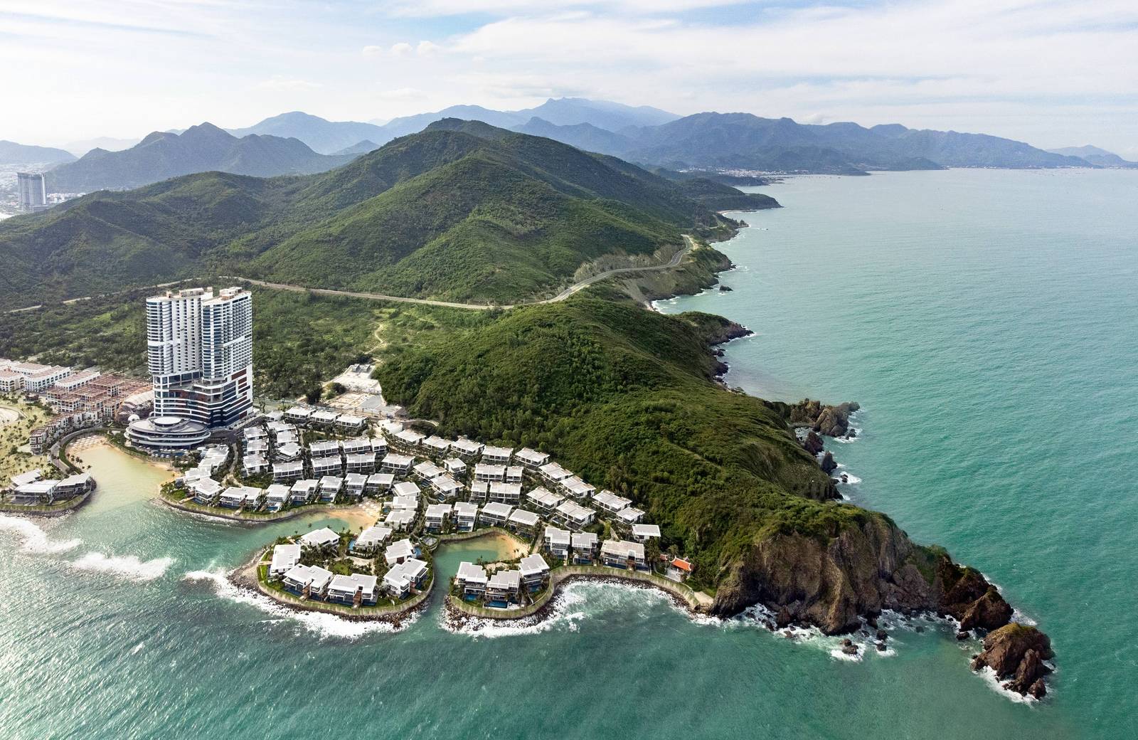 綠色山岬旁的高樓與沿海灣排開的白色別墅群空拍