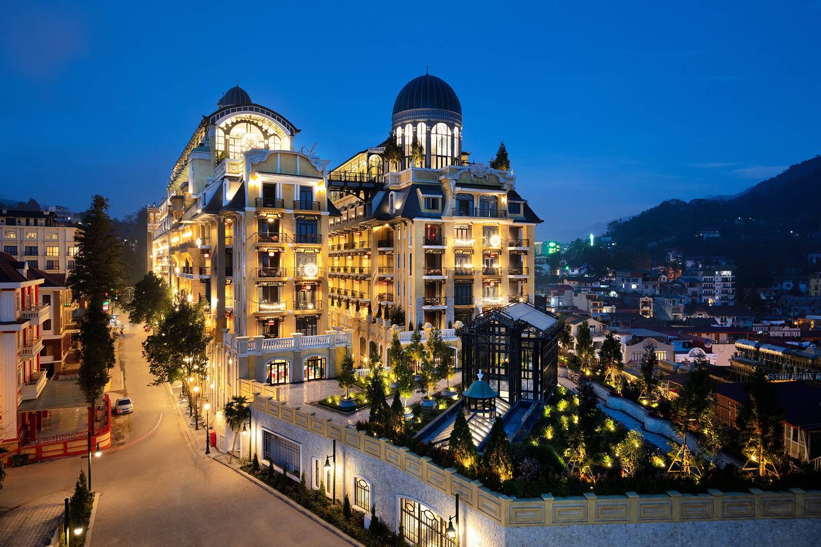 夜色中亮燈的芥末黃圓頂建築，旁邊是山城街道與遠山