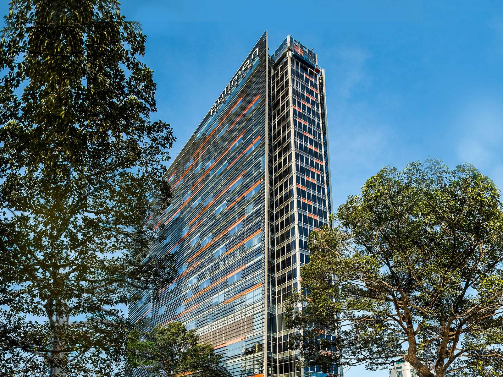 藍天下的玻璃帷幕酒店大樓與前方綠樹