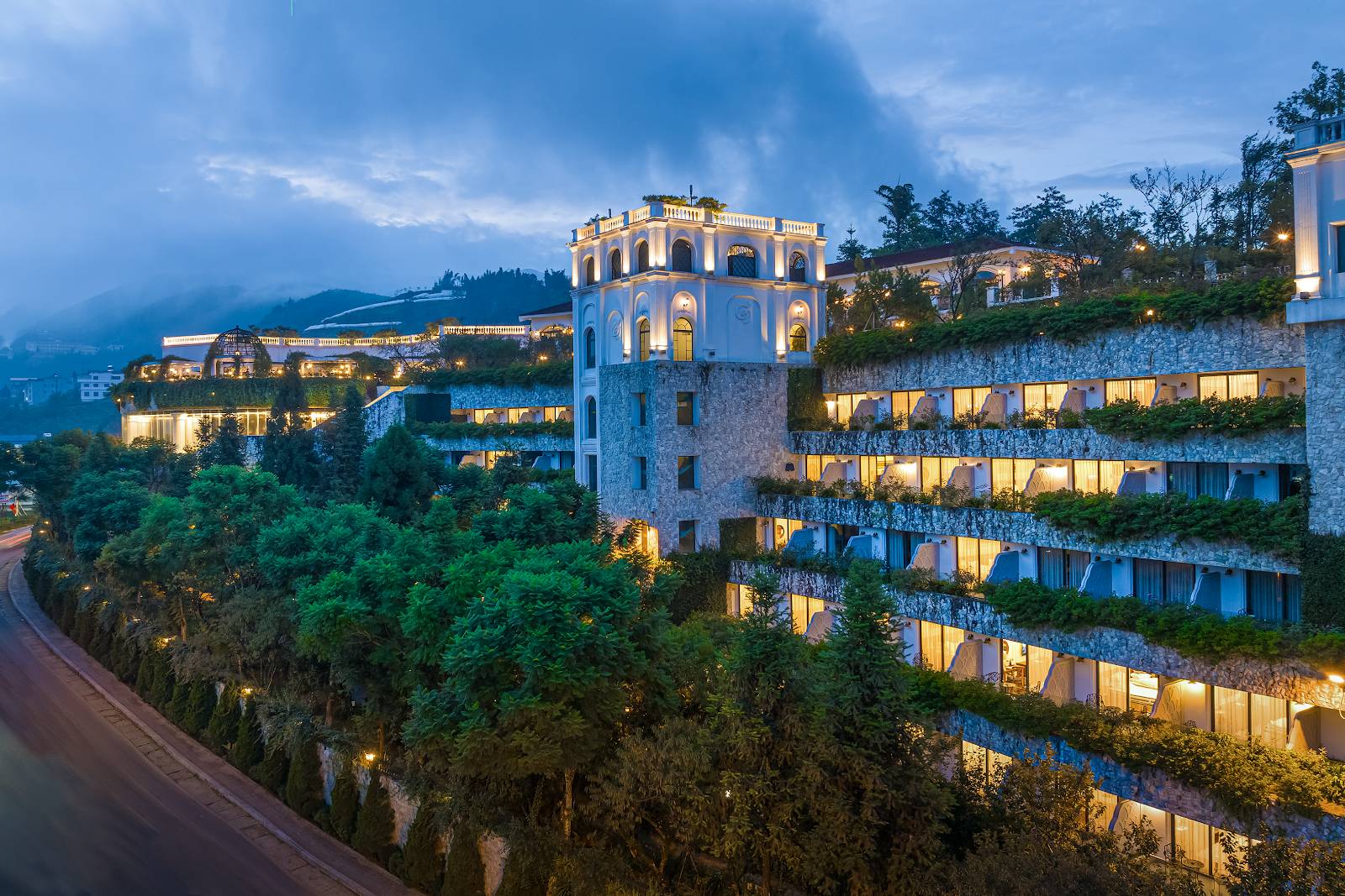 沿山坡層層退台、陽台長滿綠植的客房翼與亮燈窗戶