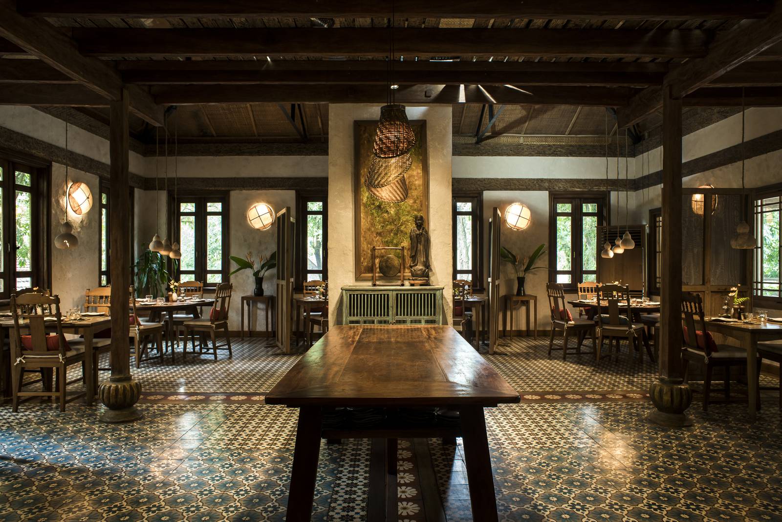 木造挑高餐廳，中央一張長桌，兩側擺著餐桌，地面鋪著花磚